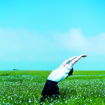 Femme levant les bras dans un champ vert, ciel bleu 