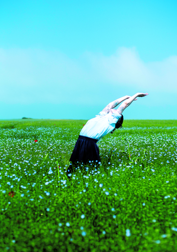 Femme levant les bras dans un champ vert, ciel bleu